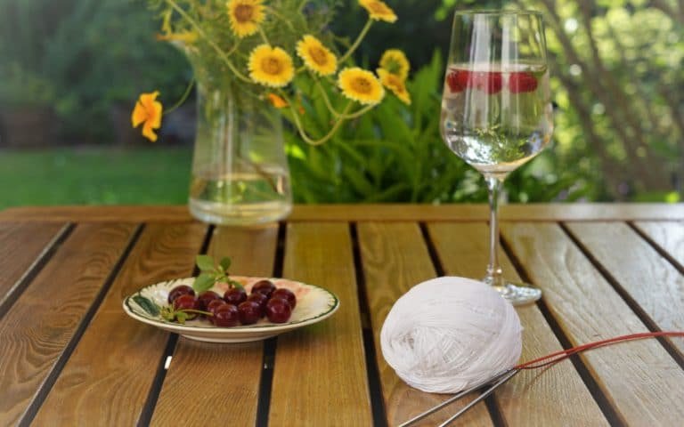 wooden table with cocktail, cherries, a wildflower bouqet and a white yarn and knitting needles on it