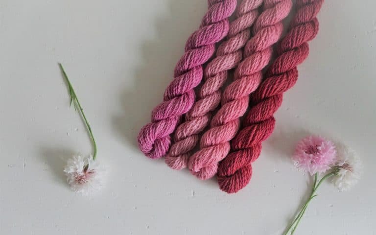 four pink mini skeins of yarn and some white and pink flowers