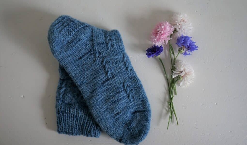 a blue hand knitted song a some flowers next to it