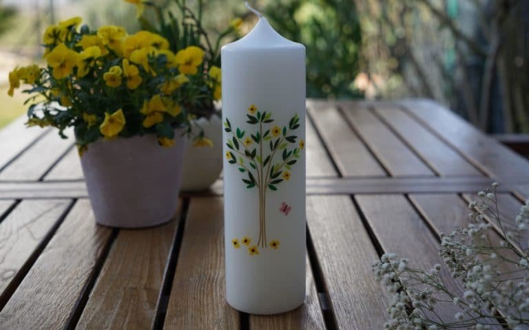 an embellished candle on a wooden table, some flowers in the fore- and background