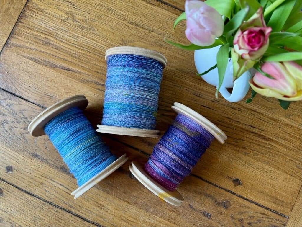 3 bobbins of handspun yarn on a table next to flowers